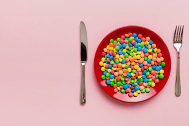 cutlery on table and sweet plate of candy. Health and obesity concept, top view on colored background.
