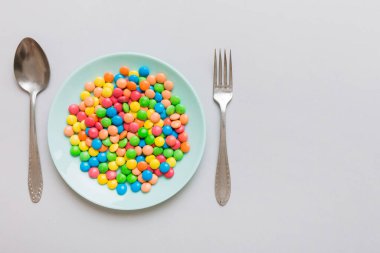 cutlery on table and sweet plate of candy. Health and obesity concept, top view on colored background.