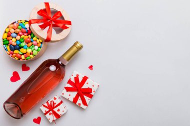 Sevgililer Günü için renkli arka planda bir şişe kırmızı şarap hediye ve çikolatalı. Kalp, hediye kutusuyla şekillendirilmiş çikolatalar fotokopi alanı ile üst görünüm.