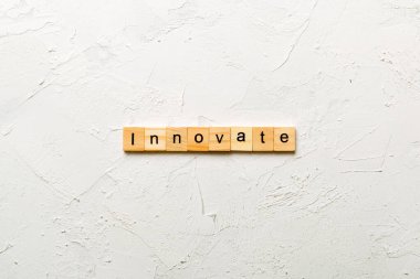 Ahşap blokta yazılmış yeni bir kelime. Çimento masasının üzerinde desing, konsept için INNOVATE metin.