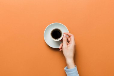 Renkli arka planda bir fincan kahve tutan minimalist stil bir kadın. Düz yerde, kapuçino bardağının üstünde. Metin için boş yer, kopyalama alanı. Kahve bağımlılığı. Üst manzara, düz uzanma.