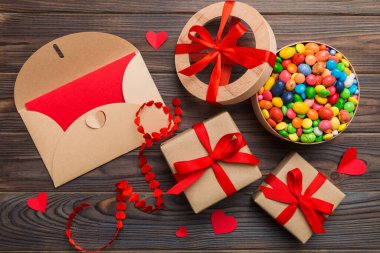 Red envelope with candy and gift box and Valentines hearts on colored background. Flat lay, top view. Romantic love letter for Holiday concept.