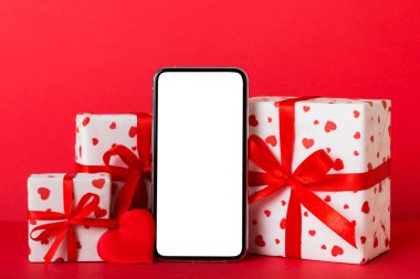 mobile phone with blank screen on colored background with hearts, calendar and gift box, valentine day concept perspertive view flat lay.