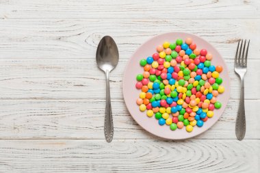 cutlery on table and sweet plate of candy. Health and obesity concept, top view on colored background.