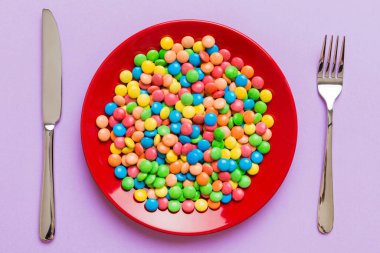 cutlery on table and sweet plate of candy. Health and obesity concept, top view on colored background.