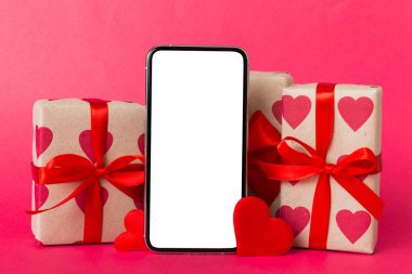 mobile phone with blank screen on colored background with hearts, calendar and gift box, valentine day concept perspertive view flat lay.