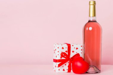 Bottle of wine on colored background for Valentine Day with gift box. Heart shaped with presrnt box perspective view with copy space.