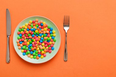 cutlery on table and sweet plate of candy. Health and obesity concept, top view on colored background.