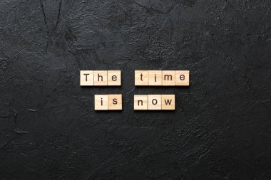 the time is now word written on wood block. the time is now text on table, concept.