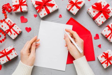 top view photo of valentine day decor female hands holding letter with envelope, small gift box and heart decoration on isolated pastel colored background with empty space.