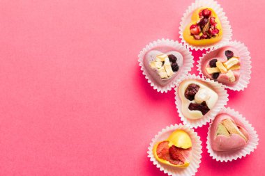 chocolate sweets in the form of a heart with fruits and nuts on a colored background. top view with space for text, holiday concept.