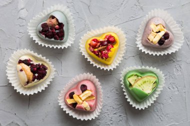 chocolate sweets in the form of a heart with fruits and nuts on a colored background. top view with space for text, holiday concept.