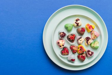 Plate with different chocolate on colored background. Assortment of fine chocolates top view vith copy space Health and obesity concept.