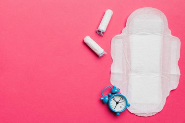 Alarm saatini hijyenik kadın tamponları ve regl pedleri ile çalıyor. Tıbbi konsept kadın kritik günler ve regl dönemi. Kadın günlük hijyen. Boşluğu kopyala.