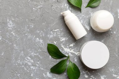 Çimento arka planında yeşil yaprakları olan organik kozmetik ürünler. Uzayı kopyala, düz yat.