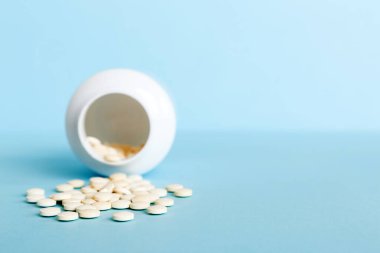 Medicine bottle and white pills spilled on a light background. Medicines and prescription pills flat lay background. White medical pills and tablets spilling out of a drug bottle.