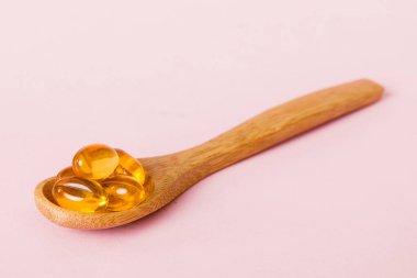 Renkli bir arka planda kaşıkta vitamin omega kapsülleri. Haplar sağlıklı bir yemek olarak sunuldu. Kırmızı yumuşak jel vitamin takviye kapsülleri kaşık üzerinde.