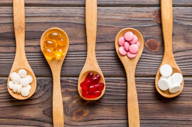 Renkli bir arka planda kaşıkta vitamin kapsülleri. Haplar sağlıklı bir yemek olarak sunuldu. Kırmızı yumuşak jel vitamin takviye kapsülleri kaşık üzerinde.
