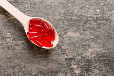 Vitamin capsules in a spoon on a colored background. Pills served as a healthy meal. Red soft gel vitamin supplement capsules on spoon.