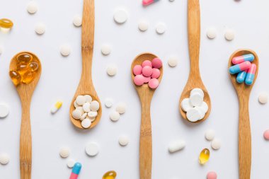 Renkli bir arka planda kaşıkta vitamin kapsülleri. Haplar sağlıklı bir yemek olarak sunuldu. Kırmızı yumuşak jel vitamin takviye kapsülleri kaşık üzerinde.