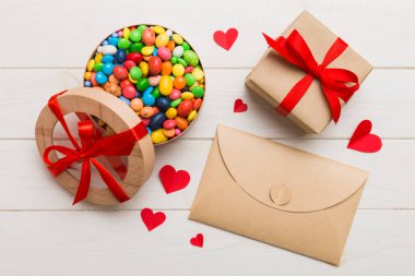 Red envelope with candy and gift box and Valentines hearts on colored background. Flat lay, top view. Romantic love letter for Holiday concept.