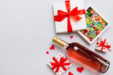 Sevgililer Günü için renkli arka planda bir şişe kırmızı şarap hediye ve çikolatalı. Kalp, hediye kutusuyla şekillendirilmiş çikolatalar fotokopi alanı ile üst görünüm.