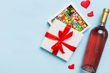 Sevgililer Günü için renkli arka planda bir şişe kırmızı şarap hediye ve çikolatalı. Kalp, hediye kutusuyla şekillendirilmiş çikolatalar fotokopi alanı ile üst görünüm.