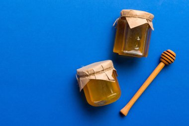 Renkli arka planda tahta çiselemeli cam bal kavanozu. Bal küpü ve dipper yükseklerde. Üst görünüm kopyalama alanı.