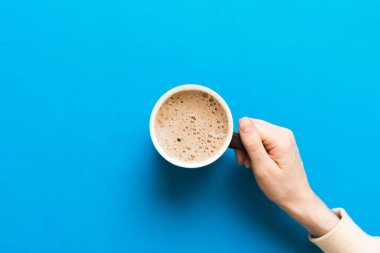 Renkli arka planda bir fincan kahve tutan minimalist stil bir kadın. Düz yerde, kapuçino bardağının üstünde. Metin için boş yer, kopyalama alanı. Kahve bağımlılığı. Üst manzara, düz uzanma.
