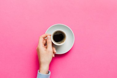 Renkli arka planda bir fincan kahve tutan minimalist stil bir kadın. Düz yerde, kapuçino bardağının üstünde. Metin için boş yer, kopyalama alanı. Kahve bağımlılığı. Üst manzara, düz uzanma.