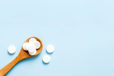 Heap of white pills on colored background. Tablets scattered on a table. Pile of red soft gelatin capsule. Vitamins and dietary supplements concept.