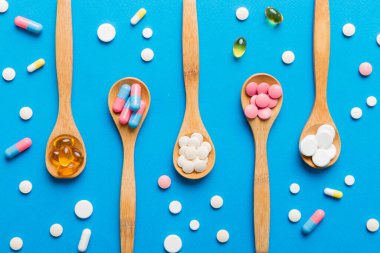 Renkli bir arka planda kaşıkta vitamin kapsülleri. Haplar sağlıklı bir yemek olarak sunuldu. Kırmızı yumuşak jel vitamin takviye kapsülleri kaşık üzerinde.