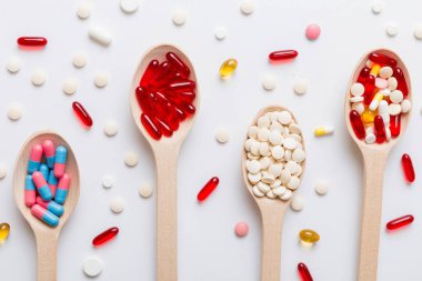 Renkli bir arka planda kaşıkta vitamin kapsülleri. Haplar sağlıklı bir yemek olarak sunuldu. Kırmızı yumuşak jel vitamin takviye kapsülleri kaşık üzerinde.