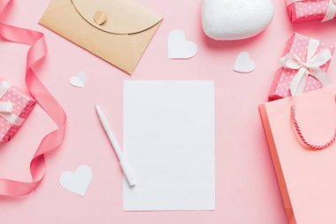 top view photo of valentine day decor female hands holding letter with envelope, small gift box and heart decoration on isolated pastel colored background with empty space.