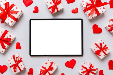 Top view of digital tablet with gift boxes and hearts on colorful background. Tablet with black screen with Holiday decorations gift box top view.