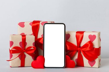 mobile phone with blank screen on colored background with hearts, calendar and gift box, valentine day concept perspertive view flat lay.