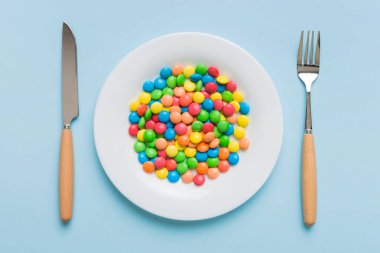cutlery on table and sweet plate of candy. Health and obesity concept, top view on colored background.
