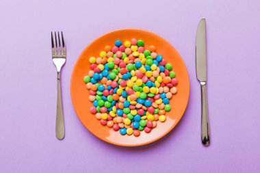 cutlery on table and sweet plate of candy. Health and obesity concept, top view on colored background.