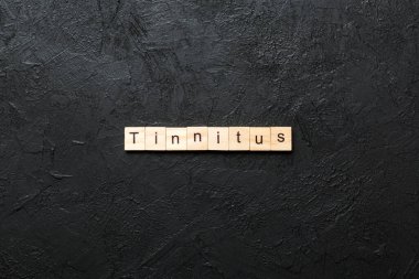 Tahta bloğa yazılmış bir kelime. Çimento sehpası üzerindeki TINNITUS metin desing, konsept.