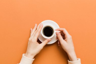 Renkli arka planda bir fincan kahve tutan minimalist stil bir kadın. Düz yerde, kapuçino bardağının üstünde. Metin için boş yer, kopyalama alanı. Kahve bağımlılığı. Üst manzara, düz uzanma.