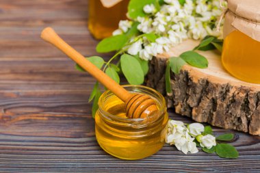 Tatlı bal kavanozu bahar akasyası çiçeklerini sarmıştı. Kavanozdaki kaşıktan bal akar. Tahta zemin üzerinde taze akasya balı kavanozları.