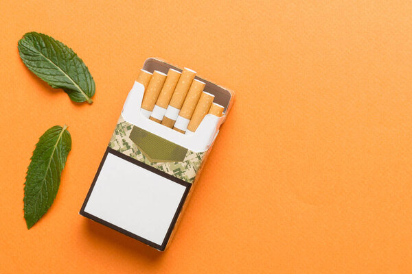 Пачка ментоловых сигарет и свежая мята на цветном столе, сигареты с ментолом сверху плоский вид.
