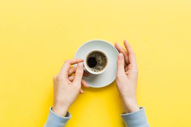 Renkli arka planda bir fincan kahve tutan minimalist stil bir kadın. Düz yerde, kapuçino bardağının üstünde. Metin için boş yer, kopyalama alanı. Kahve bağımlılığı. Üst manzara, düz uzanma.