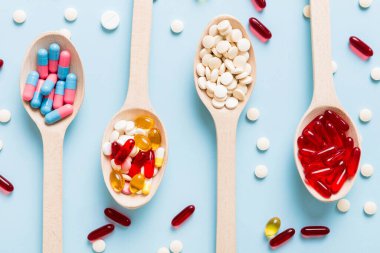 Renkli bir arka planda kaşıkta vitamin kapsülleri. Haplar sağlıklı bir yemek olarak sunuldu. Kırmızı yumuşak jel vitamin takviye kapsülleri kaşık üzerinde.