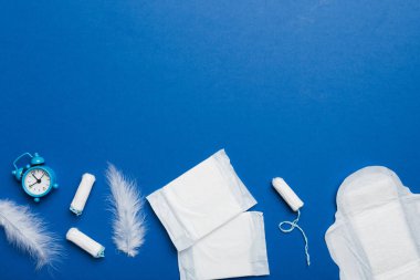 Alarm saatini hijyenik kadın tamponları ve regl pedleri ile çalıyor. Tıbbi konsept kadın kritik günler ve regl dönemi. Kadın günlük hijyen. Boşluğu kopyala.