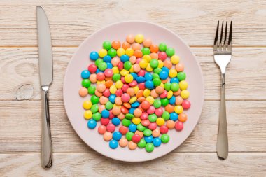 cutlery on table and sweet plate of candy. Health and obesity concept, top view on colored background.