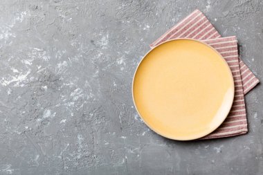 Renkli arka planda üst manzara. Yemek için masa örtüsü üzerinde boş yuvarlak sarı tabak. Tasarımınız için boşluk olan peçeteye boş tabak.