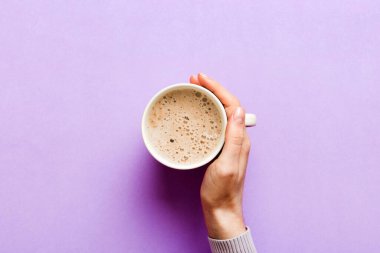 Renkli arka planda bir fincan kahve tutan minimalist stil bir kadın. Düz yerde, kapuçino bardağının üstünde. Metin için boş yer, kopyalama alanı. Kahve bağımlılığı. Üst manzara, düz uzanma.