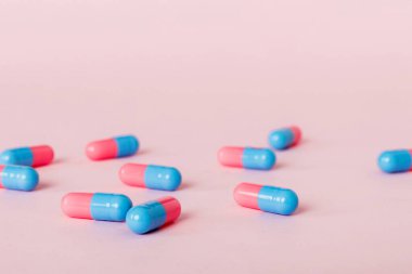 Renkli arka planda bir yığın pembe ve mavi hap. Tabletler masaya saçılmış. Kırmızı yumuşak jelatin kapsül yığını. Vitaminler ve beslenme takviyeleri konsepti.