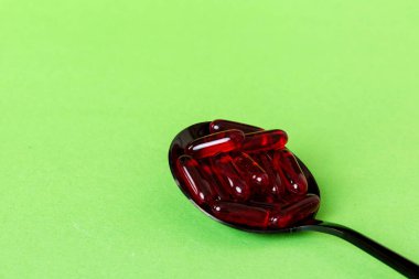 Renkli bir arka planda kaşıkta vitamin kapsülleri. Haplar sağlıklı bir yemek olarak sunuldu. Kırmızı yumuşak jel vitamin takviye kapsülleri kaşık üzerinde.
